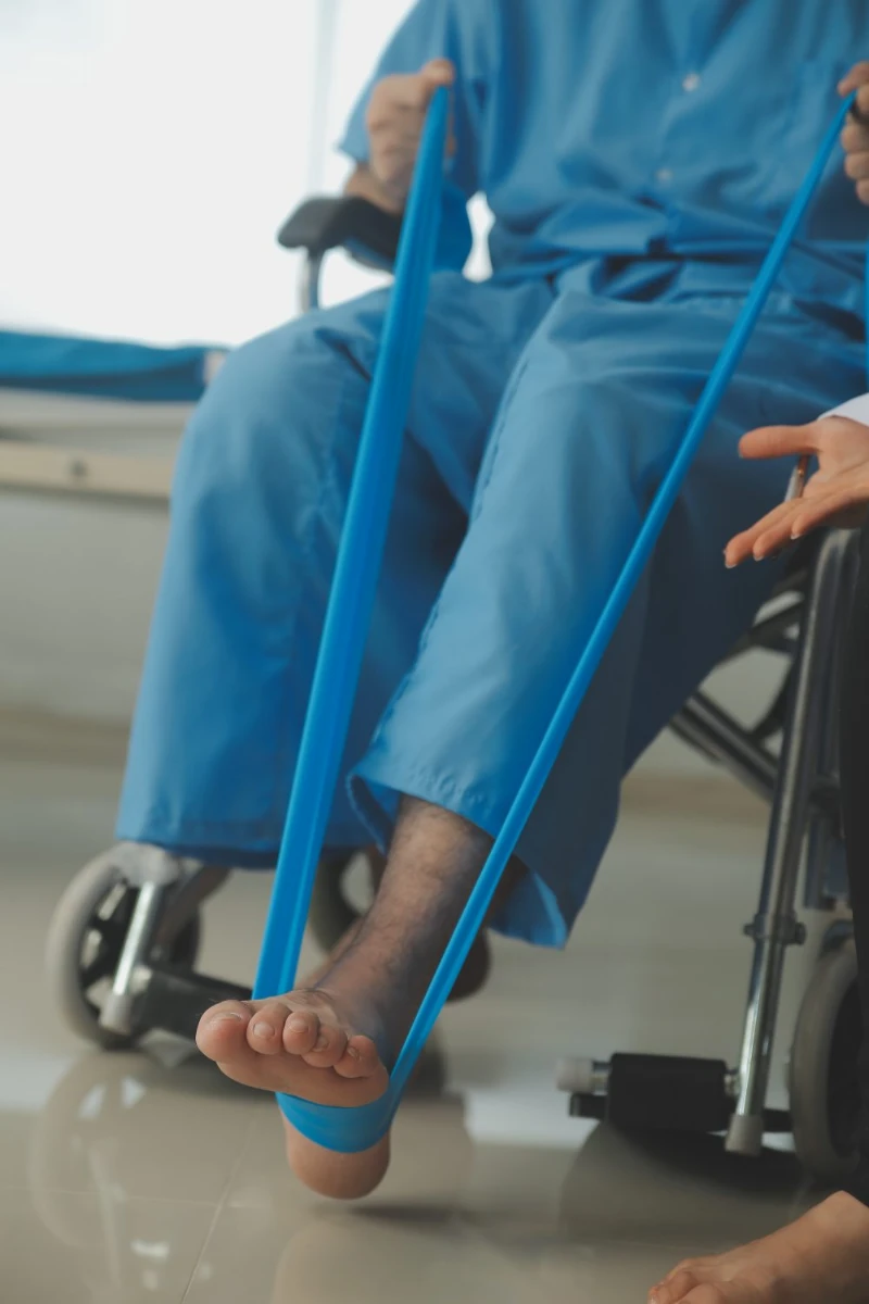 Patient in a wheelchair stretching the ankle with a blue resistance band during rehabilitation after ankle arthroscopy