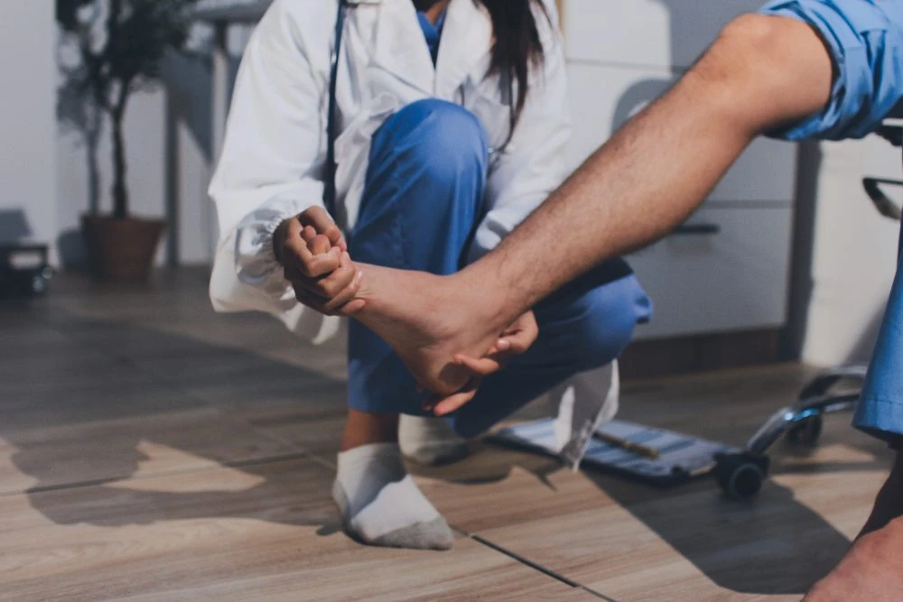 Doctor kneeling to examine a patient's bare foot and ankle in a clinic