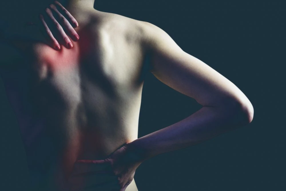 Person holding the back of their shoulder, with the painful area highlighted in red