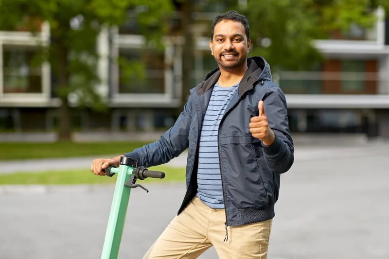 Smiling man standing with a kick scooter and giving a thumbs up outdoors