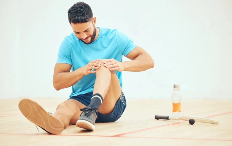 Man sitting on a sports court holding his knee